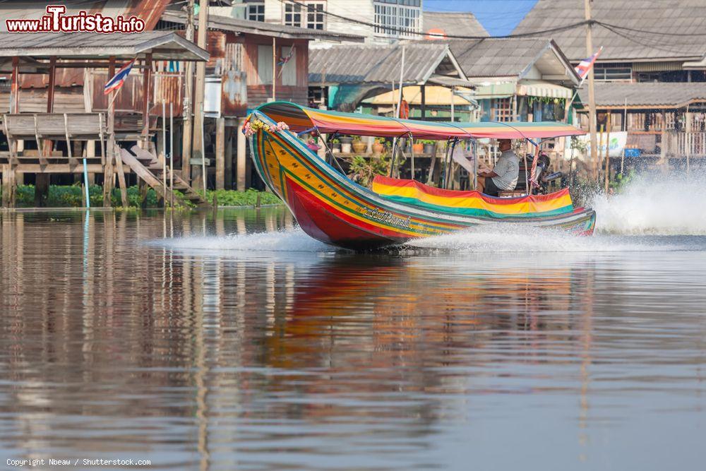 Immagine Una piroga colorata sul fiume Chao Phraya a Nonthaburi, Thailandia. Sullo sfondo, le tradizionali case thai - © Nbeaw / Shutterstock.com