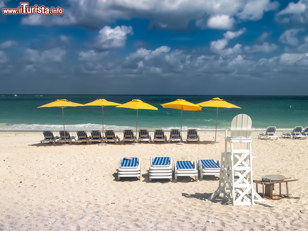 Immagine Una spiaggia di Bimini durante una giornata ventilata e nuvolosa, Bahamas. Sdraio e ombrelloni attendono i turisti che qui trovano un vero paradiso naturale dove rilassarsi e praticare attività sportive.