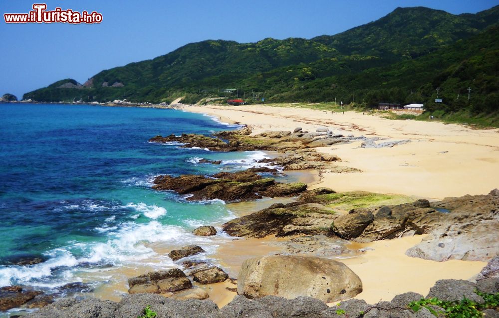 Immagine Una spiaggia di sabbia bianca sull'isola di Yakushima, Giappone. Sullo sfondo, montagne con vegetazione rigogliosa.