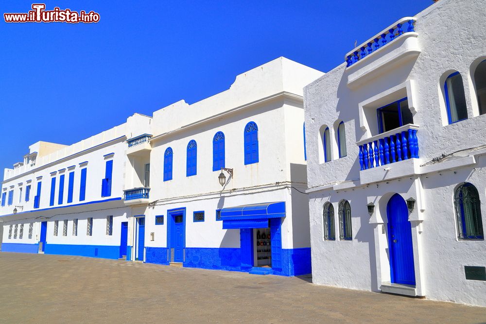 Immagine Una strada di Asilah fotografata con il sole, Marocco. A risplendere sono il cielo azzurro e i particolari blu delle facciate delle abitazioni.