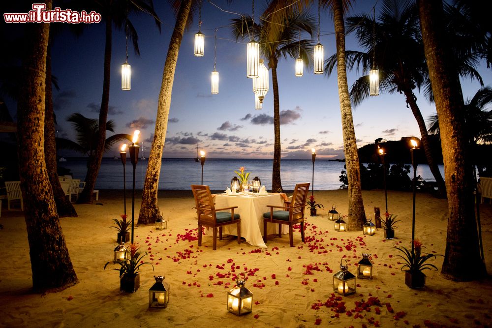 Immagine Una tavola apparecchiata in spiaggia sull'isola di Antigua, America Centrale. A rendere più suggestiva l'atmosfera già romantica sono la luce delle lanterne e i petali rossi sparsi sulla sabbia dorata.