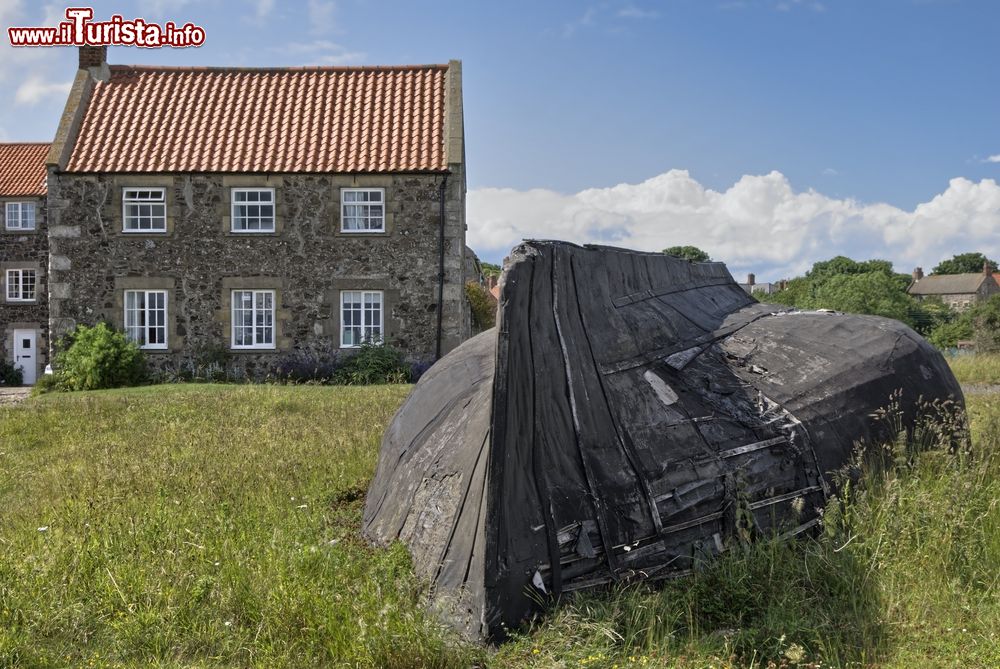 Immagine Una tipica barca in legno rovesciata su un prato a Lindisfarne, Inghilterra. Sullo sfondo, eleganti edifici in pietra.