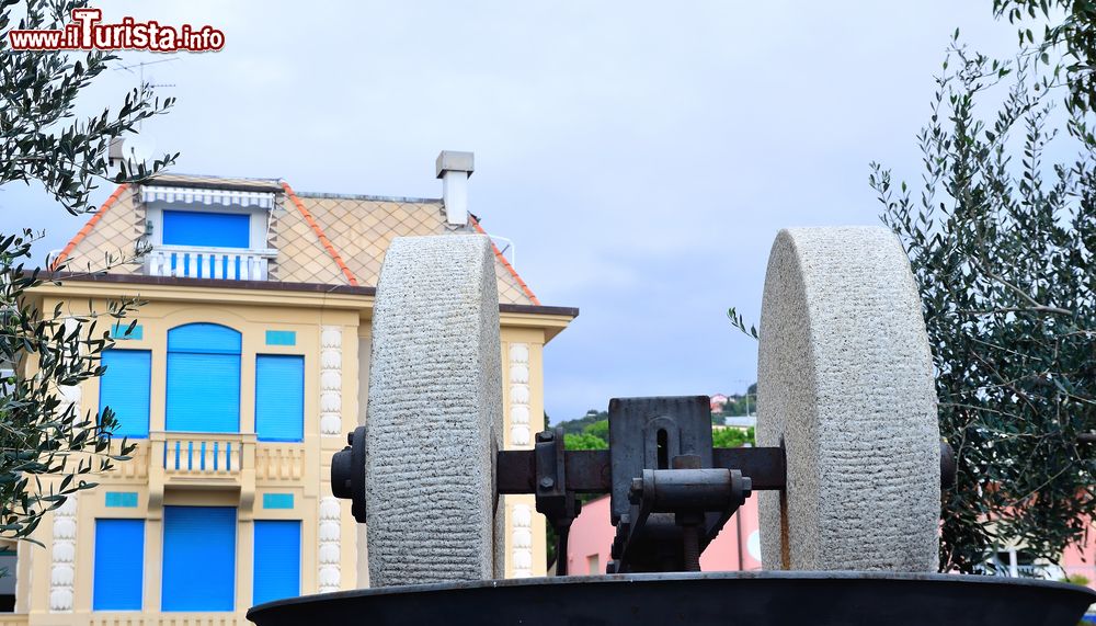 Immagine Una vecchia macina di fronte a un edificio dalle finestre azzurre e blu a Celle Ligure, Liguria.