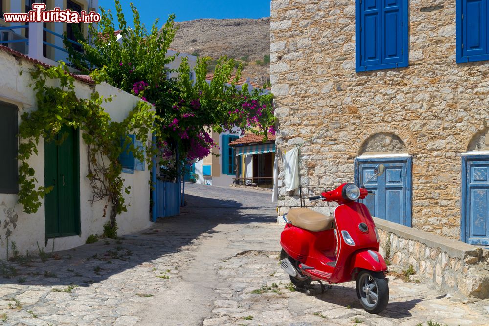Immagine Una viuzza dell'isola di Chalki, Grecia, con una vespa color rosso parcheggiata.