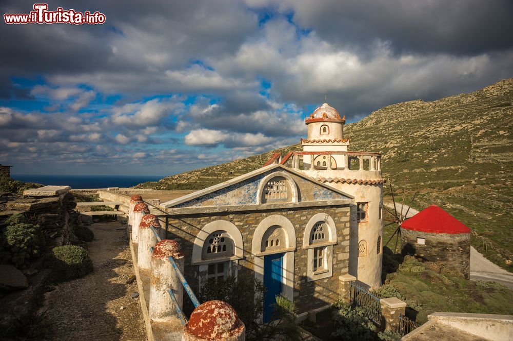 Immagine Un'antica chiesetta lungo la strada per la città di Isternia, isola di Tino, Grecia. A fianco, un tradizionale mulino a vento con il tetto rosso.