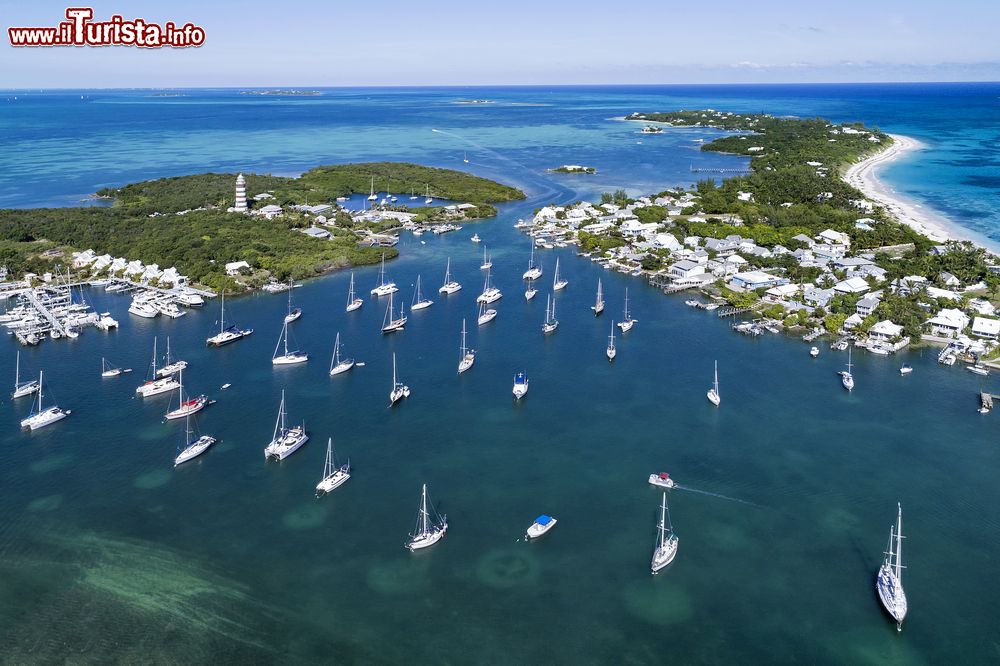 Immagine Veduta aerea del porto e del faro da Hope Town su Elbow Cay, isole di Abaco, Bahamas. Questo isolotto, popolato in origine da britannici in fuga dagli Stati Uniti d'America nel 1785, è sopravvissuto alla pesca e alla costruzione di imbarcazioni. Il villaggio principale di Hope Town è protetto da un famoso faro a strisce bianche e rosse che si innalza per 37 metri. Venne costruito nel 1863.