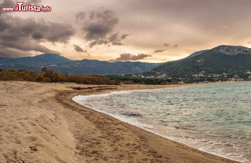 Immagine Veduta panoramica della spiaggia di Algajola, Corsica, con rocce e sabbia e il villaggio sullo sfondo.