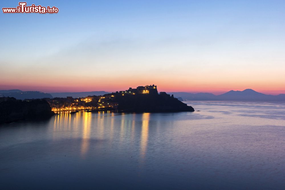 Immagine Veduta serale della Marina della Corricella a Procida con il  Vesuvio sullo sfondo, Campania. Siamo nel borgo marinaro più antico dell'isola, disposto ad anfiteatro sul mare: questo porticciolo secentesco è famoso per la sua architettura caratteristica.