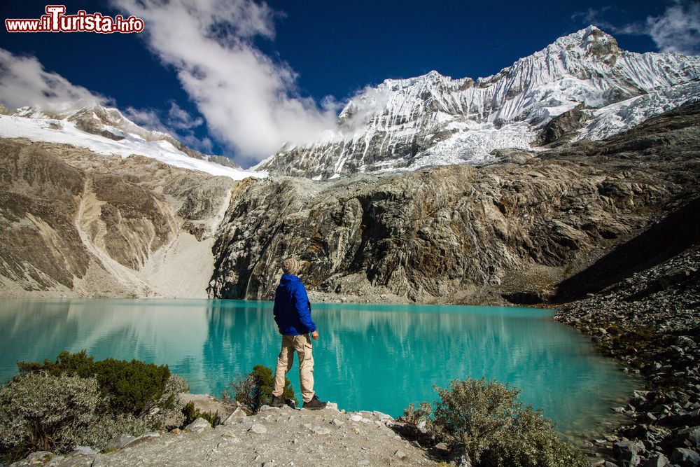 Immagine Un viaggiatore avventuroso con zaino in spalla contempla la laguna dai 69 colori allo Huascaran National Park, Huaraz, Perù. Sullo sfondo, la grande montagna Chacraraju innevata. Il parco nazionale è stato istituito nel 1975 e si estende per 158 chilometri da sud a nord con una larghezza media di 20 km.