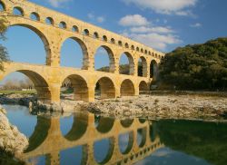 Riflessi sulle acque del fiume Gardon: è l'inconfondibile silhouette dello storico Pont du Gard, l'antico acquedotto romano che si trova a Vers, in Liguadoca-Rossiglione, nel ...