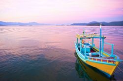 Un tramonto struggente nella baia di Paraty: una barca di un pescatore nella luce calda ed arrossata della sera in Brasile - © ostill / Shutterstock.com