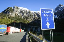 Cartello stradale in direzione di Salzburg-Villach con camion parcheggiati a lato strada, Flachau (Asutria) - © Goran Jakus / Shutterstock.com