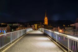 Il ponte sul fiume Drava fotografato di notte a Villach, Austria. Sullo sfondo, la torre campanaria illuminata.

