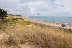 Kite surfing su una spiaggia deserta dell'isola di Ré, Francia. Dune di sabbia ricoperte di erba caratterizzano questo lembo di terra.

