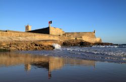 La spiaggia di Oeiras con il forte Sao Juliao da Barra, Portogallo. Fotografata con la luce del sole, la fortezza del XVI° secolo riflette la sua sagoma sulla sabbia umida.


