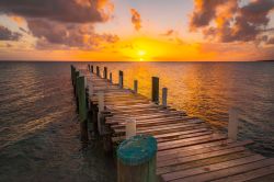 Un molo in legno fotografato durante il tramonto sull'isola di Eleuthera, Bahamas. I riflessi dorati del cielo si rispecchiano sull'acqua del mare e sulla passerella dove attraccano ...