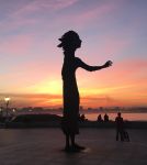 Monumento alle madri dei migranti sulla passeggiata di Gijon, Spagna: una suggestiva veduta della scultura in bronzo fotografata al tramonto - © Francisco Cidoncha / Shutterstock.com