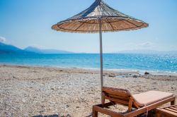 Ombrellone e lettino sulla spiaggia di Qeparo, con sabbie, ciottoli e mare pulito.