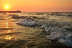 Onde del mare al tramonto sulla spiaggia di Jesolo, Veneto. Sullo sfondo, un pescatore sul pontile.


