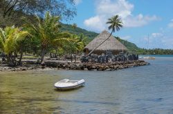 Paesaggio costiero sulle rive del lago salato di Fauna Nui con un'imbarcazione e una tradizionale capanna in paglia, isola di Huahine, Polinesia Francese.

