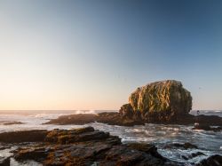 Panorama di Punta de Lobos, Cile, con il tramonto e un surfista pronto a tuffarsi in acqua.

