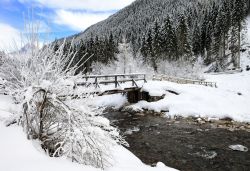 Un ponte in legno coperto di neve attraversa il torrente Biois nei pressi di Falcade, Veneto.



