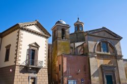 Scorcio della chiesa dei Santi Martiri a Tuscania, Lazio. La facciata ottocentesca si presenta con un ampio arco sorretto da due robusti piedritti e in alto un finestrone.
