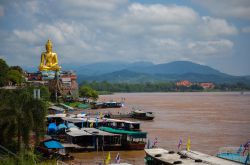 Statua dorata di Buddha a Chiang Saen, Thailandia. In primo piano, barche ormeggiate sull'acqua fangosa  - © opportunity_2015 / Shutterstock.com