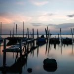 Tramonto su un molo in legno e sulle barche a Rosolina, Veneto. 
