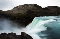 Un corso d'acqua con cascata a Puerto Natales, Cile. A fare da scenario, un paesaggio aspro e selvaggio.
