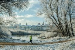 Un uomo fa jogging in un parco innevato di Varsavia, Polonia. Sullo sfondo, la skyline della capitale.
