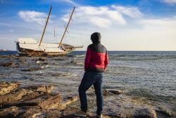 Un uomo osserva una barca naufragata dalla costa di Calasetta, Sardegna.



