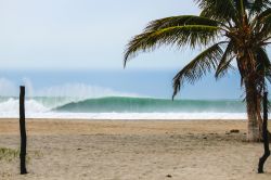 Una grande onda s'infrange sulla spiaggia di Puerto Escondido, Messico, in una giornata nuvolosa.

