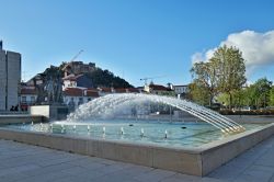 Una piazza con fontana nel centro della città di Leiria, Portogallo: sullo sfondo, il castello merlato che domina dall'alto di una collina.
