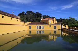 Una storica fabbrica di polvere da sparo a Oeiras, Portogallo. L'edificio si riflette nello stagno del giardino sotto un cielo con qualche nube.


