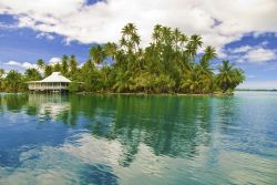 Uno splendido scorcio della laguna dell'isola di Huahine, Polinesia Francese. Sullo sfondo, palme da cocco e una tradizionale capanna in legno.
