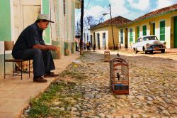 Un uomo con una gabbietta per gli uccelli in una strada di Trinidad, Cuba - è una tipica scena di vita quotidiana a Trinidad, quella che possiamo osservare in questa foto, scattata in ...