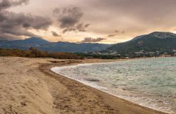 Veduta panoramica della spiaggia di Algajola, Corsica, con rocce e sabbia e il villaggio sullo sfondo.

