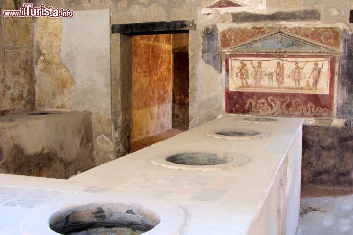 Immagine Thermopolium Asellina di Pompei, Campania - E' la locanda più completa rinvenuta a Pompei. Durante gli scavi archeologici è stata riportata alla luce una grande quantità di suppellettili di cui parte in terracotta e parte in bronzo. All'esterno della struttura, un'insegna mostra tre brocche e un imbuto con al di sopra un'iscrizione eletttorale in cui si dice che le "aselline" Maria, Egle e Smyrina appoggiavano l'elezione di tale Lollio Fusco. Il nome Asellina, con cui ancora oggi viene chiamato il thermopolium, era probabilmente quello della proprietaria della locanda © JeniFoto / Shutterstock.com