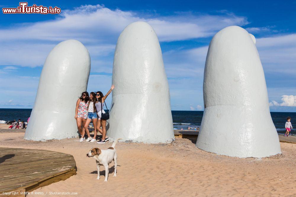 Immagine Tre ragazze in posa per una foto vicino a La Mano, Punta del Este (Uruguay): la celebre scultura è opera dell'artista Mario Irarrazabal e si trova a Playa La Brava - © RUBEN M RAMOS / Shutterstock.com
