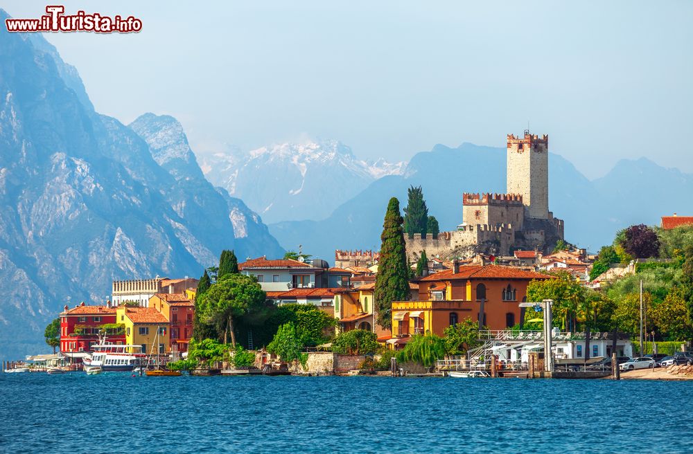 Immagine La città di Malcesine affacciata sul Garda, Veneto. Il castello e la torre cittadina con le montagne innevate sullo sfondo e le tipiche case colorate che si affacciano sul lago.