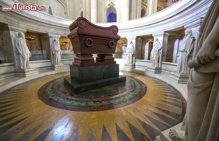 Immagine La Tomba di Napoleone racchiusa nella Cappella dell'Hotel des Invalides, Parigi (Francia) - Come si può vedere dall'immagine, la tomba di Napoleone I è circondata da statue, ma non si tratta di sculture marmoree qualsiasi bensì delle 12 vittorie, che simboleggiano le campagne militari del condottiero. Il fatto che sia adagiata su un piedistallo non particolarmente fastoso, il suo color terra bruciata di Siena apparente nonostante il materiale sia composto di quarzite rosa, il pavimento che ricorda nel disegno la simbologia del sole, famoso elemento che ha dato anche il soprannome di Luigi XIV, pone lo spettatore di fronte a una situazione aulica altissima - © photogolfer / Shutterstock.com