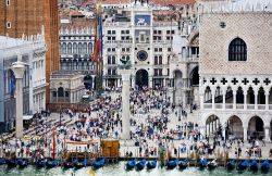 I turisti affollano Piazza e piazzetta San Marco in una giornata di sole. Si notano il Palazzo Ducale a destra, le due colonne, la base del Campanile di San Marco e la torre dell'Orologio ...