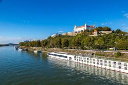 Il fiume Danubio con le imbarcazioni ormeggiate sulla banchina in primo piano e, sullo sfondo, la collina sulla quale svetta il castello di Bratislava - foto © S-F / Shutterstock.com ...