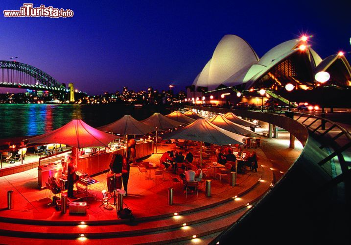 Immagine Fotografia notturna della baia di Sydney e dell'Opera House, Australia - Una suggestiva immagine dell'Opera House, definita da molti un capolavoro dell'architettura moderna, e della piccola penisola al centro della città di Sydney dove sorge. La struttura si trova a nord del Giardino Botanico Reale e a poco meno di 800 metri dalla stazione ferroviaria di Circular Quay.
