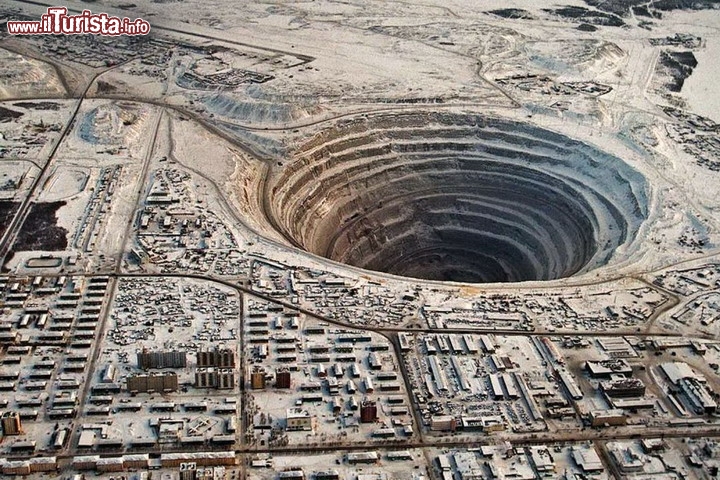 Miniera di diamanti a Mirny, Russia - A vederla dall'aereo sembra una città uscita da un film di fantascienza! Mirny (Mirnyj) in Jacuzia, repubblica autonoma della Russia,  è famosa per la sua miniera di diamanti, che ha creato una incredibile voragine, che assomiglia al cratere di uno schianto meteorico. Ad altri la miniera sembra una rappresentazione dell'inferno dantesco, con i gironi che si intrudono nel sottosuolo come un gigantesco imbuto di roccia. Pensate che la voragine è arrivata fino a 1200 metri di profondità, ma ora la ricerca dei diamanti prosegue in galleria, e gli scavi sono terminati. Il volo degli elicotteri sopra alla miniera è interdetto: la miniera agisce come un grande aspirapolvere e nel passato ha aspirato un paio di velivoli, facendoli precipitare.