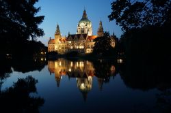 Il Neues Rathaus di Hannover (Germania) illuminato in una foto serale, dove si può apprezzare il riflesso sulle acque del laghetto Maschteich.