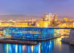 L'esterno del MuCEM illuminato alla sera e, sullo sfondo, la città di Marsiglia (Francia) - © vichie81 / Shutterstock.com