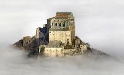 La Sacra di San Michele si erge sopra un manto di nuvole in Val di Susa, ad ovest di Torino - © Elio Pallard, CC BY-SA 4.0, Wikipedia