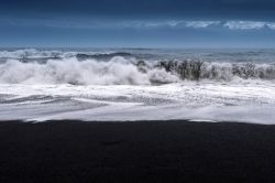 Il mare impetuoso si abbatte sulla sabbia nera della spiaggia ai piedi del promontorio di Dyrholaey (Vik, Islanda).
